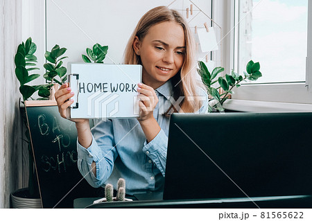 Young female teacher sitting at desk and using laptop showing HOMEWORK text at home. e Education Back to school. Student learning online class. Distance learning. Exam preparation 81565622