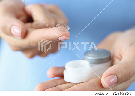 Woman holds contact lens and storage container on finger closeup 81565859
