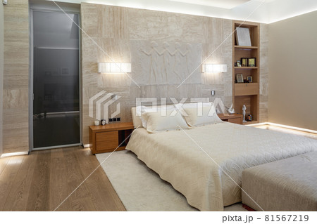 Bedroom with double bed near marble wall with sculptural panel and wall sconces 81567219