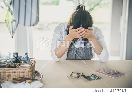 女性が部屋で電卓とお金を出して頭を抱えている　woman money 81570854