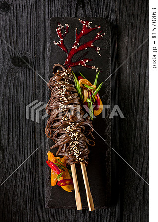 soba noodles of buckwheat Noodles of buckwheat yellow and red pepper, herbs. Pan-Asian cuisine. On stone tray on dark wooden table. 81570863