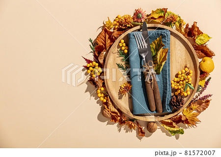 Autumn thanksgiving table place setting with cutlery, wooden plate and arrangement of fall leaves 81572007