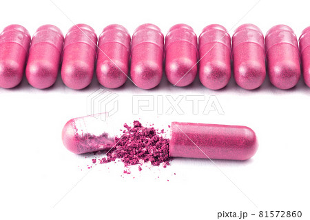 row of plastic pink color organic capsules isolated on white background closeup with one opened 81572860