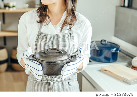 キッチンで女性がミトンをつけて両手で鍋を持っている　woman kitchen 81573079