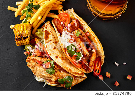 First corn tortilla with grilled chicken fillet, second with fish fillet, french fries, sauce and beer on black backgroud 81574790