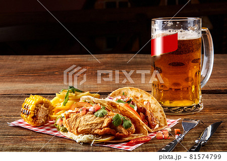 First corn tortilla with grilled chicken fillet, second with fish fillet, sauce and beer on wooden table First corn tortilla with grilled chicken fillet, second with fish fillet, sauce and beer on wooden table 81574799