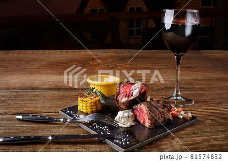 Barbecue steak with a glass of red wine as close-up on black board on wooden background Barbecue steak with a glass of red wine as close-up on black board on wooden background 81574832