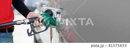 Gas station worker in red uniform filling up bronze pickup truck tank. Closeup hand holding green gas pump nozzle. 81575655