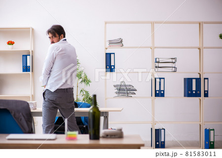 Young alcohol addicted employee sitting in the office Young alcohol addicted employee sitting in the office 81583011