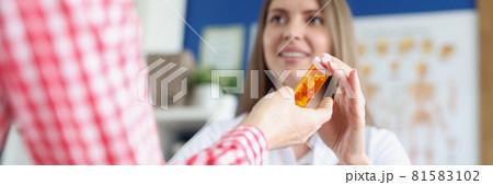 Woman doctor giving jar of capsules to patient in hands in clinic closeup Woman doctor giving jar of capsules to patient in hands in clinic closeup 81583102
