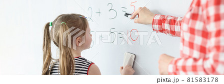 Little girl and teacher solving math equations on blackboard Little girl and teacher solving math equations on blackboard 81583178