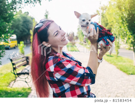 The girl holds a mini chihuahua in her arms. Kissing your pet. The dog and the owner are dressed in the same color. Clothes for animals. Love and care for four-legged pets. The girl holds a mini chihuahua in her arms. Kissing your pet. The dog and the owner are dressed in the same color. Clothes for animals. Love and care for four-legged pets. 81583454