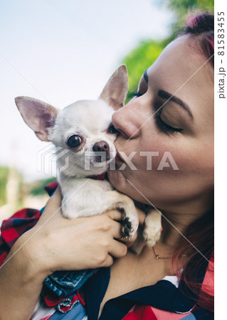The girl holds a mini chihuahua in her arms. Kissing your pet. The dog and the owner are dressed in the same color. Clothes for animals. Love and care for four-legged pets. 81583455