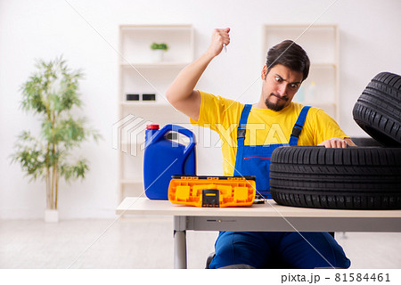 Young male garage worker with tyre at workshop Young male garage worker with tyre at workshop 81584461