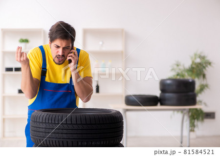 Young male garage worker with tyre at workshop 81584521
