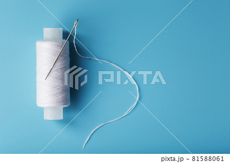 A spool of white thread with a needle on a blue background. 81588061
