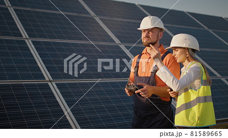 Industrial expert wearing helmet and controlling drone in photovoltaic solar power plant. Solar panel array installation. Technologies and ecology. Female investor checks the work Industrial expert wearing helmet and controlling drone in photovoltaic solar power plant. Solar panel array installation. Technologies and ecology. Female investor checks the work 81589665