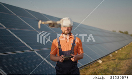 Industrial expert wearing helmet and controlling drone in photovoltaic solar power plant. Solar panel array installation. Technologies and ecology. Female investor checks the work 81589673