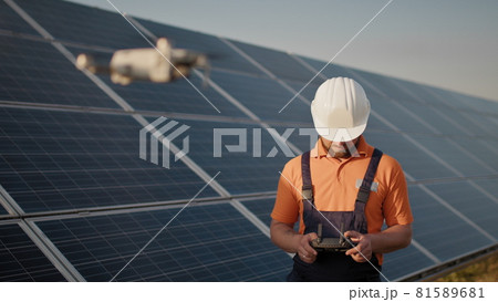 Industrial expert wearing helmet and controlling drone in photovoltaic solar power plant. Solar panel array installation. Technologies and ecology. New technologies Industrial expert wearing helmet and controlling drone in photovoltaic solar power plant. Solar panel array installation. Technologies and ecology. New technologies 81589681