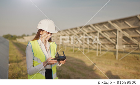 Engineer woman in hardhat holding tablet computer operating flying drone in solar plant. Photovoltaic solar panel installation. Solar array. New technologies. The investor checks the solar power Engineer woman in hardhat holding tablet computer operating flying drone in solar plant. Photovoltaic solar panel installation. Solar array. New technologies. The investor checks the solar power 81589900