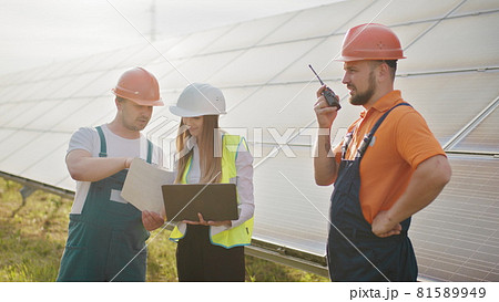 Team of industrial colleagues using tablet monitoring rows of photovoltaic solar panels at sunset. Business cooperation. Solar park. Alternative energy concept. Clean energy 81589949