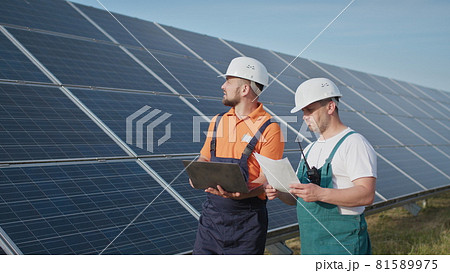 Energy specialist using digital tablet reading information to check the efficiency of solar panel construction. Green energy jobs. Technology. Two solar power plant workers are recording data 81589975
