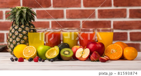 Different fruits juice in glass, apple, orange and strawberry juice with straw, looking refreshing on colourful wood board in front of brick wall background. Picture decorating with fresh fruits Different fruits juice in glass, apple, orange and strawberry juice with straw, looking refreshing on colourful wood board in front of brick wall background. Picture decorating with fresh fruits 81593874