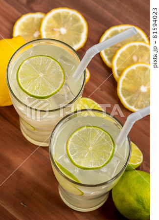 Two refreshing glasses of cold fruit juice with straw, ice lime and lemon juice, decorating with fresh lime and lemon on wooden table. Concept for refreshing 81594023