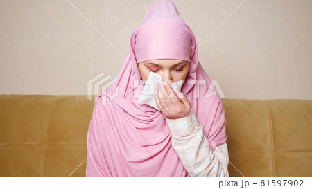 Beautiful muslim woman in hijab coughs and freezes while sitting on the sofa 81597902