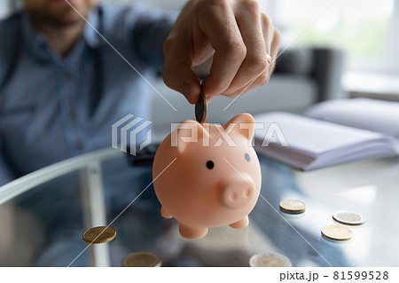 Millennial man inserting coin into piggy bank 81599528