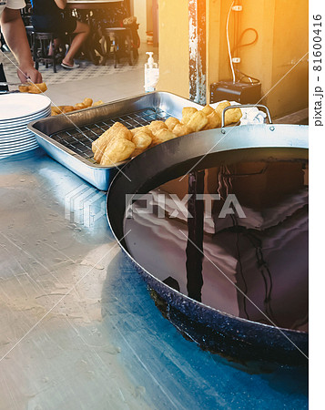 Dough sticks or deep-fried Chinese dough called patongo for sale on tray near large frying pan. Patongo is a deep-fried dough stick. Famous traditional asian breakfast street food. Selective focus. 81600416