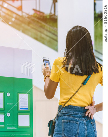 Back view of female customer wear face mask registering with smartphone and scan QR CODE via SafeEntry to check-in during the outbreak of Corona virus(Covid-19) at the entrance gate.New normal concept 81600816