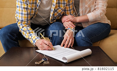 Husband signs apartment purchase contract near wife on sofa 81602115
