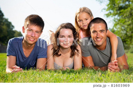 Happy parents with two kids laying on grass in sunny summer park 81603969