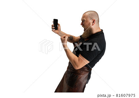 Comic portrait of muscular bearded bald man, blacksmith in leather apron or uniform isolated on white studio background. Concept of labor, retro professions, power, beauty, humor Comic portrait of muscular bearded bald man, blacksmith in leather apron or uniform isolated on white studio background. Concept of labor, retro professions, power, beauty, humor 81607975