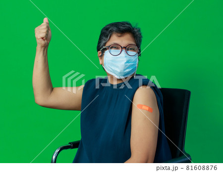 Asian middle age woman wearing protective hygiene mask showing bandage on arm looking to camera with happy trust and confidece after getting vaccine for protect coronavirus or covid-19 81608876