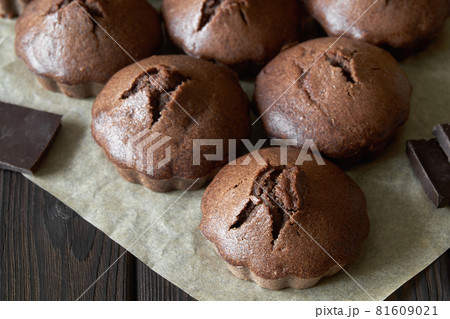 A group of homemade chocolate muffins on parchment with pieces of chocolate. Dark wooden background, closeup, selective focus 81609021