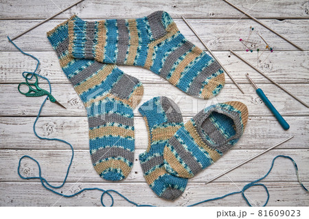 Two children's knitted socks and slippers on a light wooden background 81609023