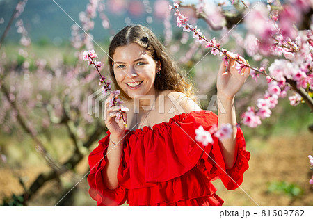 Woman in red dress standing near blooming peach tree 81609782