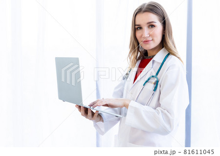 female doctor with stethoscope working with laptop computer and writing on paperwork on wooden table in Hospital background 81611045