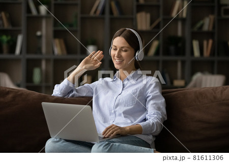 Smiling woman in headphones waving hand at webcam, using laptop Smiling woman in headphones waving hand at webcam, using laptop 81611306
