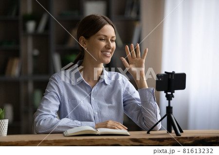 Smiling woman waving hand, using smartphone on tripod, recording video Smiling woman waving hand, using smartphone on tripod, recording video 81613232