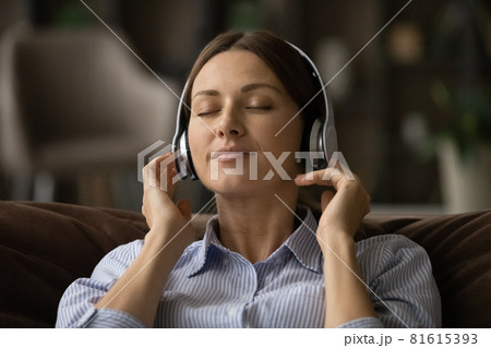 Head shot peaceful woman in headphones enjoying music on couch 81615393