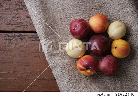 Juicy fruits in a linen tablecloth on a old wooden table. Plums, apricots on a dark red background. Top view. Juicy fruits in a linen tablecloth on a old wooden table. Plums, apricots on a dark red background. Top view. 81622446