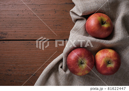 Fruits in a linen tablecloth on a old wooden table. Apples on a dark red background. Apple harvest theme. Place for text, top view 81622447