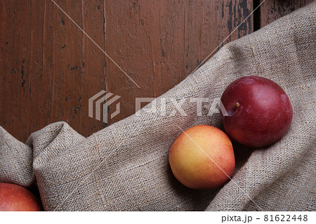 Juicy fruits in a linen tablecloth on a old wooden table. Apples, plums, apricots on a dark red background. Top view. Juicy fruits in a linen tablecloth on a old wooden table. Apples, plums, apricots on a dark red background. Top view. 81622448