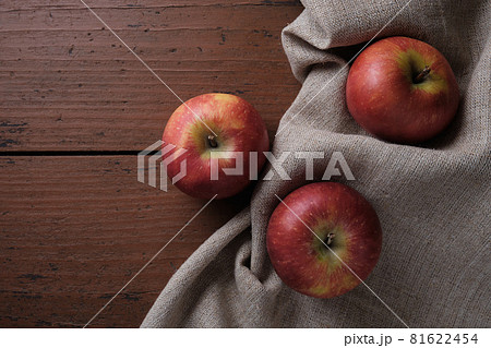 Fruits in a linen tablecloth on a old wooden table. Apples on a dark red background. Apple harvest theme. Place for text, top view Fruits in a linen tablecloth on a old wooden table. Apples on a dark red background. Apple harvest theme. Place for text, top view 81622454