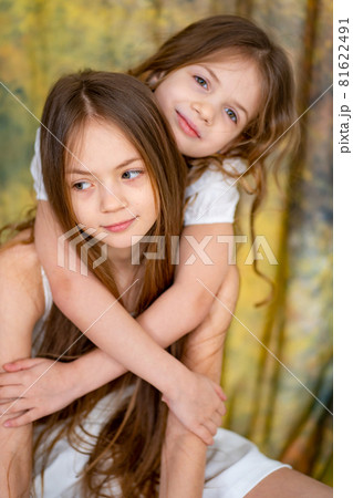 two little girls with long hair in white clothes cuddle. love between sisters. two little girls with long hair in white clothes cuddle. love between sisters. 81622491