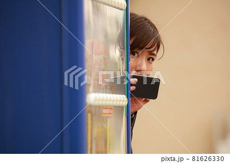 自動販売機の陰からスマートフォンで写真を撮る女性 81626330
