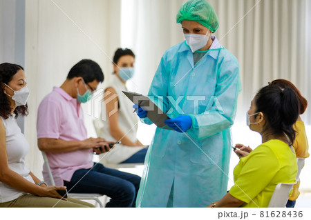 Group of diverse citizens wear face mask in Coronavirus vaccinating queue line sitting checking his personal information from paper board in hands of full protection suit doctor Group of diverse citizens wear face mask in Coronavirus vaccinating queue line sitting checking his personal information from paper board in hands of full protection suit doctor 81628436